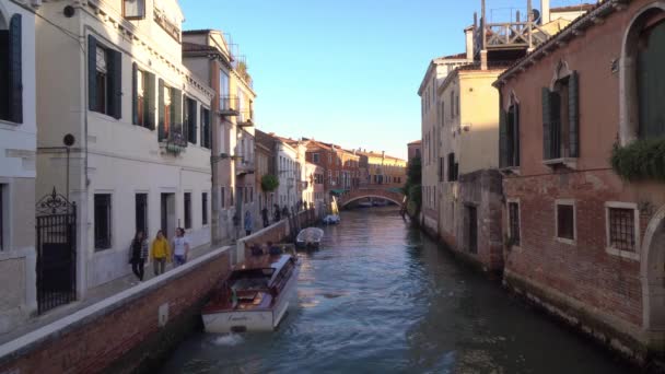 Boote schwimmen auf einem der vielen kanäle in venedig italien, während touristen durch die engen gassen streifen — Stockvideo