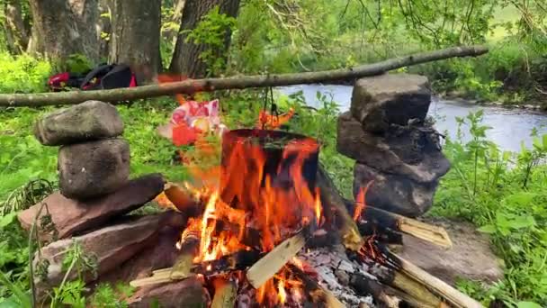 Cocinar comida al aire libre en la olla turística en la hoguera. Proceso de preparación de alimentos para acampar en el fuego ardiente mientras camina a la naturaleza salvaje — Vídeos de Stock