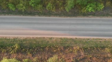 Tarlalar arasındaki yolda hava uçuşu. Sonbahar renkleri. Yeşil kırsal alan ve araba geçiyor. Beyaz bir arabanın arkasında ve yanında uçarken güneş parlayan yeşil doğaya rağmen