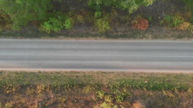 Tarlalar arasındaki yolda hava uçuşu. Sonbahar renkleri. Yeşil kırsal alan ve araba geçiyor. Mavi bir arabanın arkasında ve yanında uçarken, yeşil doğayla birlikte güneş parlarken