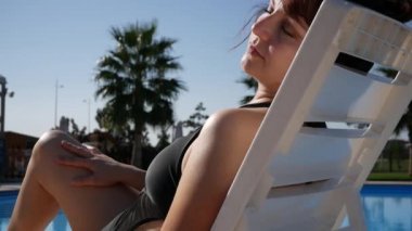 Beach Resort Hotel'de yaz gününün tadını çıkaran kadın, pürüzsüz depilated bacaklara dokunuyor. Havuz başında güneşlenen kadın.