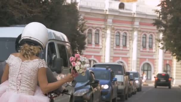 Recién casados conducen por la ciudad en motocicleta a través del tráfico en la ciudad de verano. La novia está celebrando un ramo de bodas. Joven hermosa pareja paseos por las calles de la ciudad — Vídeos de Stock