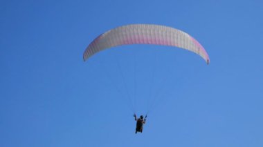 Açık mavi gökyüzüne karşı uçan aşırı yamaç paraşütü, güneş ışınları kameraya parlar. Yamaç paraşütle uçuş deneyimi skydive yaz.