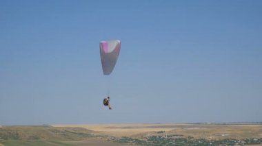 Açık mavi gökyüzüne karşı uçan aşırı yamaç paraşütü, güneş ışınları kameraya parlar. Yamaç paraşütle uçuş deneyimi skydive yaz.