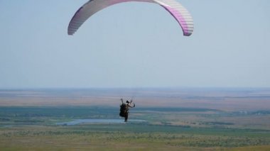 Açık mavi gökyüzüne karşı uçan aşırı yamaç paraşütü, güneş ışınları kameraya parlar. Yamaç paraşütle uçuş deneyimi skydive yaz.