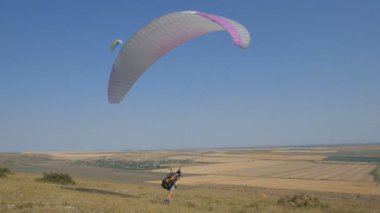Açık mavi gökyüzüne karşı uçan aşırı yamaç paraşütü, güneş ışınları kameraya parlar. Yamaç paraşütle uçuş deneyimi skydive yaz.
