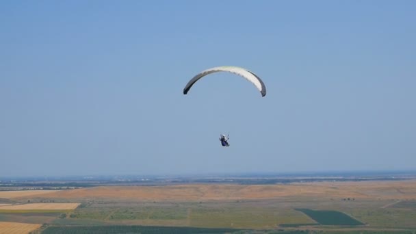 Açık mavi gökyüzüne karşı uçan aşırı yamaç paraşütü, güneş ışınları kameraya parlar. Yamaç paraşütle uçuş deneyimi skydive yaz. — Stok video