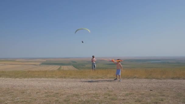 Een jongen rent langs de weg met een vlieger. Droom van vliegen, kinderspel. Jongens op een achtergrond van blauwe lucht — Stockvideo