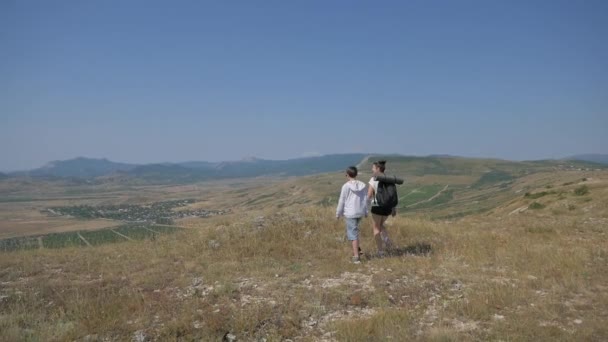 Mother and son travel together in mountains, they go to the edge of a cliff in grass covered barren mountain landscape — ストック動画