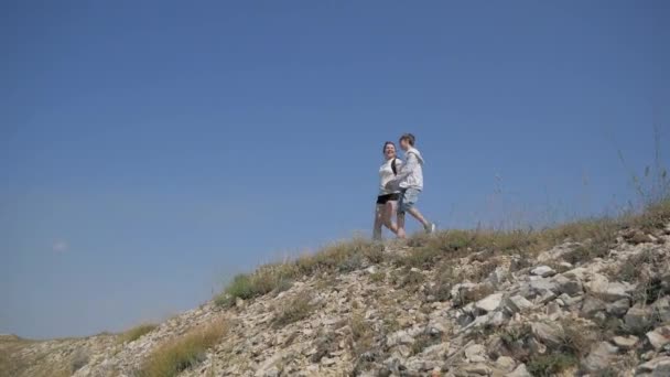 Мать и сын путешествуют вместе в горах, они идут к краю скалы в траве покрытой бесплодной горной пейзаж — стоковое видео