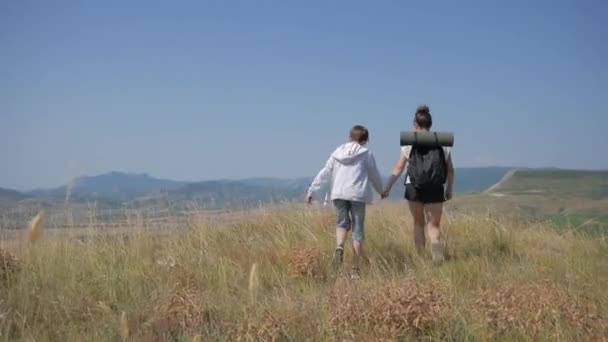 Madre e hijo viajan juntos en las montañas, van al borde de un acantilado en el paisaje de montaña estéril cubierta de hierba — Vídeos de Stock