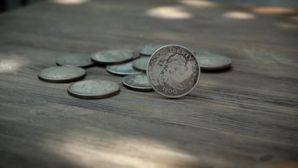 Monedas de plata estadounidenses cayendo en cámara lenta sobre una madera, girando a medida que aterrizan y, finalmente, se establecen — Vídeo de stock