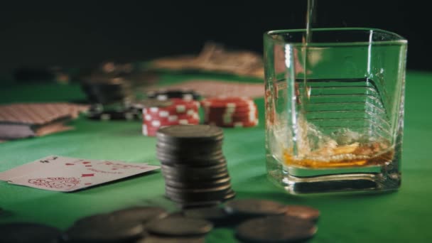 Whisky of rum wordt langzaam in een glas gegoten, en dan worden ijsblokjes gegooid. Casino Poker Chips, munten en dek van het spelen van kaarten gestapeld in meerdere stapels op tafel. Gokfortuin — Stockvideo