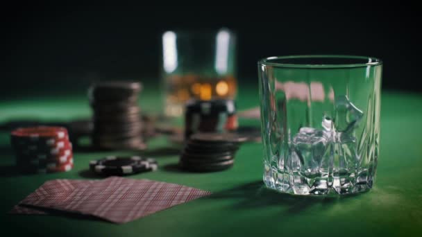 Os cubos de gelo caem lentamente no copo e, em seguida, o uísque ou rum é derramado. Casino Poker Chips, Moedas e Deck de jogar cartas empilhadas em várias pilhas na mesa. Sorte de jogo — Vídeo de Stock