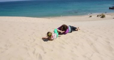 komik dört yaşında sarışın kız haddeleme ve kumul Bolonia Beach, Cadiz, Endülüs, İspanya, Avrupa içinde iplik oynayan kadın annesi ile yalan