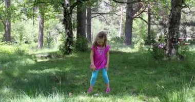 Dört yaşında sarışın kız kırsal bir ormandaki Frizbi oynamaya çimenlerin üzerinde ayakta. 4k video.