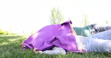 Üç yıl yaşlı sarışın çocuk ve kadın anne yeşil yalan gizle oynarken çayır, çimen ve genel Park Juan Carlos, Madrid İspanya mor havlu ile aramak