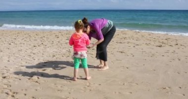 dört yaşında çocuk ya da kız ve seyir için toplama ve deniz kabukları, kum plaj sahil Bolonia Beach, Cadiz, Endülüs, İspanya, Avrupa'nın toplama anne.