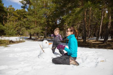 Mutlu bir aile. Burun, ormanın yanında kış doğada olarak havuç ile bir kardan adam ile oynarken dizleri üstünde oturan anne ve dört yıl yaşlı sarışın çocuk kadın,