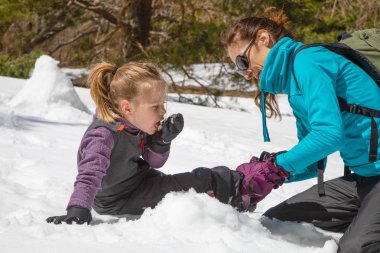 önyükleme için komik onun kızı, dört yaşında sarışın kız, doğada kar üzerinde oturan yerleştirerek bir kadın. Çocuk kar eliyle yiyor