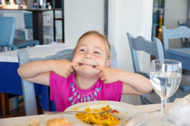 İspanyol paella pirinç yeme restoranda oturan ağzını germe palyaçoluk yaparken dört yaşında sarışın kız portresi