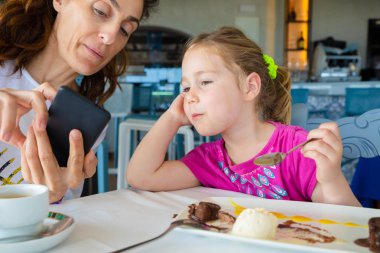 Anne gösteren cep telefonu kızı dört yaşında sarışın beyaz kız, tatlı restoranda yemek için