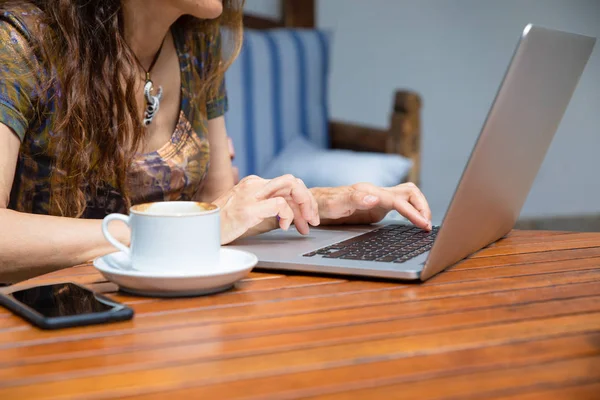 女性手在电脑笔记本电脑键盘上打字的细节 在棕色木桌上用咖啡杯和黑色手机空白屏幕 — 图库照片