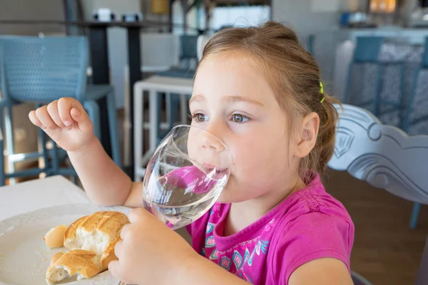 Nelivuotias Blondi Pieni Tyttö Vaaleanpunainen Paita Juomavesi Cup Istuu Sisätiloissa — kuvapankkivalokuva