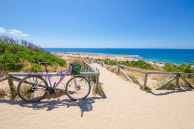 Canos fırlayan Köyü (Barbate, Cadiz, Endülüs, İspanya), mavi gökyüzü yakınındaki Cape Trafalgar, okyanus kıyılarında aşağı kum geçit Access'te plaj yanındaki mor Bisiklet Park