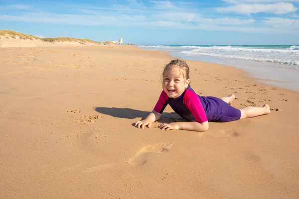 快乐的四岁女孩 小冲浪者与氯丁橡胶冲浪服 躺在沙滩上 微笑着看着 在帕尔马海滩 加的斯 安达卢西亚 西班牙 — 图库照片