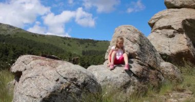 Four years old blonde girl sitting over rock and stones, playing and speaking, in the countryside of Guadarrama, Madrid, Spain, Europe. 4k video