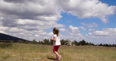Dört yaşında sarışın kız bir şube veya sopa ile oynayan ve bir taş ya da kırsal kesimde anne yanındaki taş atma çayırda yürüyüş. 4k video