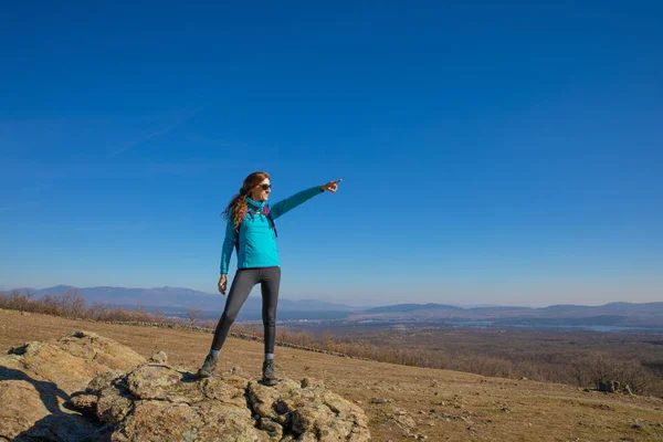 Mujer excursionista de pie sobre roca en la montaña de Madrid señalando con ha — Foto de Stock