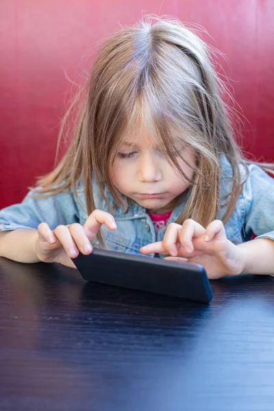 Kis gyermek megható okostelefon ül piros kanapé és fekete-t — Stock Fotó