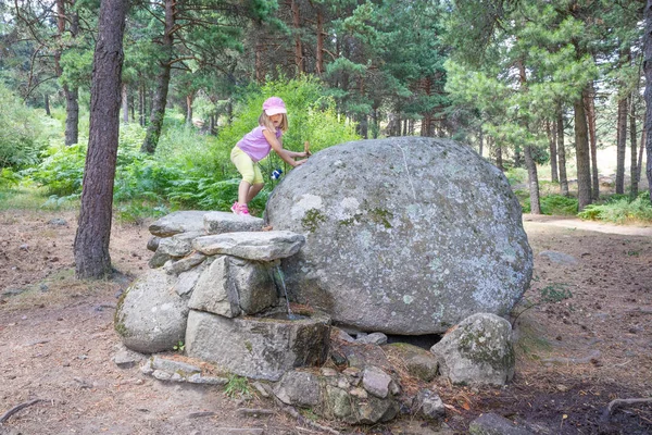 Klein meisje wandelen op rotsen boven een fontein in het bos van M — Stockfoto