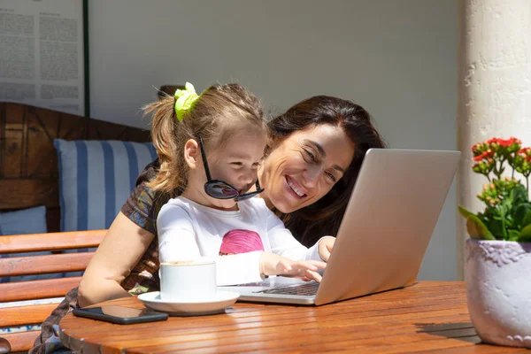 Funny little girl and mother laughing typing on laptop — Stock Photo, Image