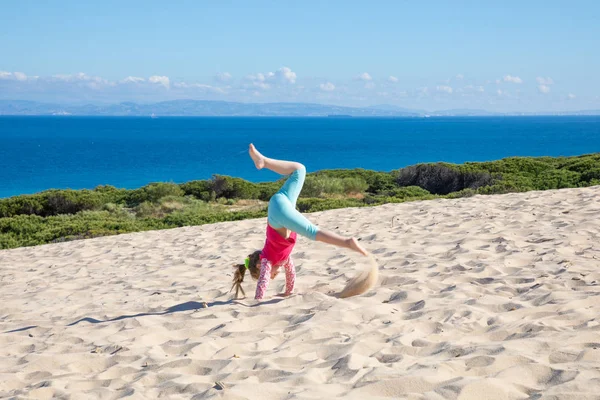 Mädchen macht Handstand auf Düne mit Afrika am Horizont — Stockfoto