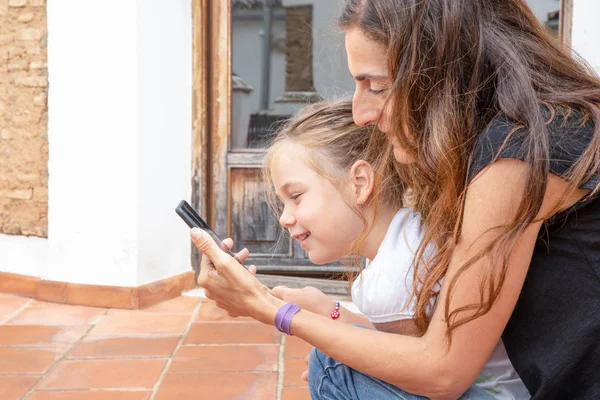 Little girl and woman watching mobile and smiling — Stock Photo, Image