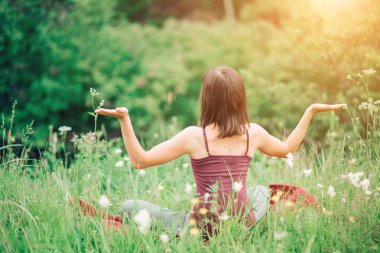 Geri ile oturan genç kadın elleri güneşli bir yaz aylarında doğada açın. Sağlık, yoga, meditasyon, uyum, sakin ol kavramı