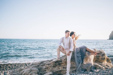Güzel çift gelin ve damat sırt sırta ve gülümseyerek oturan deniz yakınlarında. Aşk, mutluluk, Düğün