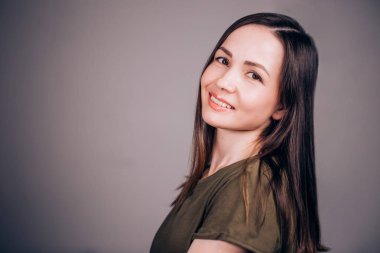 Yatay gri bir arka plan üzerinde genç bir esmer kadın portresi kapatın. Kız kameraya bakarak çekici bir gülümseme ile