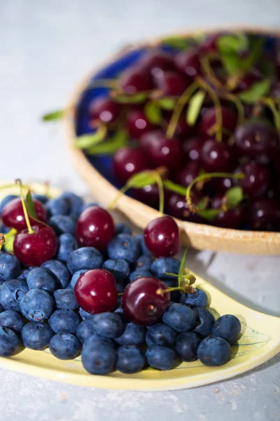 Wild berries in bowls - blueberry, cherry on a gray background close up