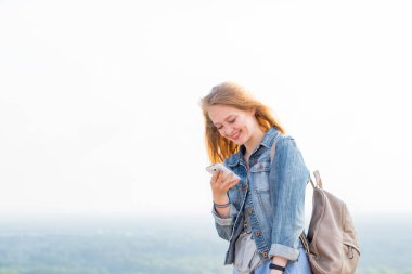 İletileri okurken, internette smartphone üzerinden bir şey izliyor ve doğada gülümseyen mutlu genç kadın. yatay dikey, kopya alanı