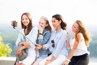 Neşeli grup genç gülümseyen kadın doğa arka plan üzerinde bir selfie stick kullanarak bir selfie yapar