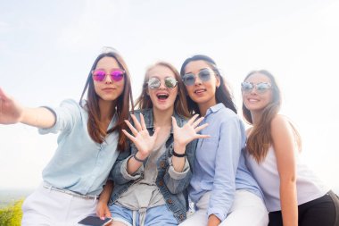 Arkadaşlarım parkta yürürken selfies al. Dört güzel kadın güneş gözlüğü takıyor günün iyi geçiyor