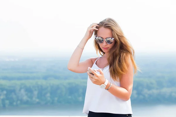 サングラスで美しい若い女性は 山の中のスマート フォンを使用します 現代の技術 アプリケーション インターネット 携帯電話 通信の概念 — ストック写真