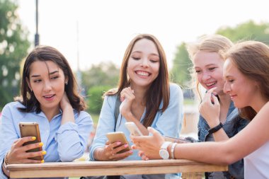 Komik kız bir akıllı telefon kullanmak ve bir yaz kafe masada gülmek