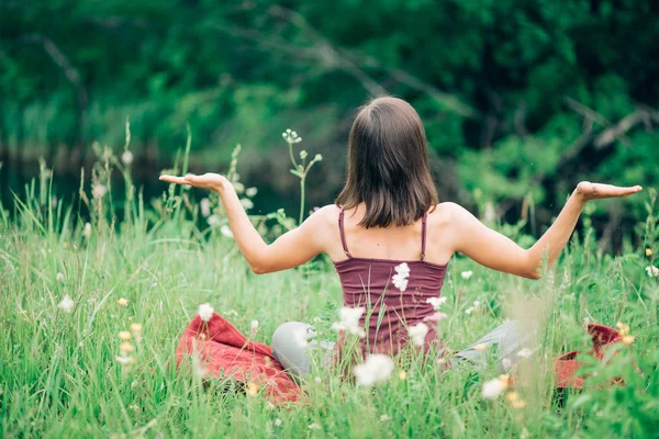 Young woman sitting back with her hands open in nature in the summer