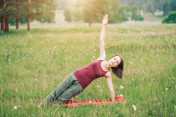 Young woman practicing yoga on the background of fields and forests in summer. Health, sport, happiness concept