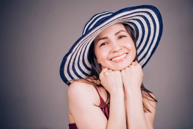 Neşeli gülümseyen kadın çizgili şapka ve eli çeneme tutar. Mutluluk, pozitif duygular, sakin ol kavramı